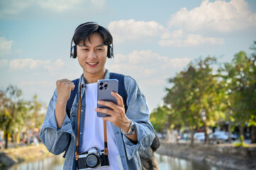 Cheerful male traveler holding his smartphone and showing clenched fist while strolling in the city.
