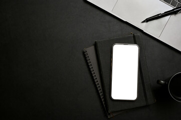 Black workspace with smartphone mockup, notepad, laptop, pen and copy space. top view