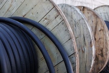 Large spool of black thick electrical wire or cable. Wooden reel with electrical industrial wires at a construction site. 