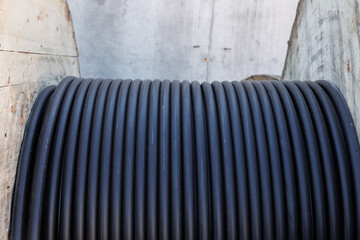 Large spool of black thick electrical wire or cable. Wooden reel with electrical industrial wires at a construction site. 