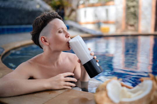 A beautiful woman in the pool drinks a milkshake from freshly made coconut banana and milk. Healthy food and rest.