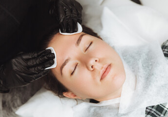 Fototapeta na wymiar A cosmetologist does a cosmetic facial massage for a relaxed young woman's face in a beauty spa. Facial care, massage, skin care, cosmetology concept