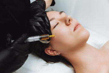 A cosmetologist performs plasmolifting on the face of a beautiful woman in a beauty salon. The...