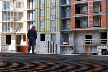 The foreman is standing at the construction site. The civil engineer observes the construction of the volume against the backdrop of the construction site. 