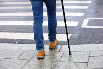 Man walking with a cane on crosswalk. Male legs in jeans on pedestrian crossing, street safety - obrazy, fototapety, plakaty