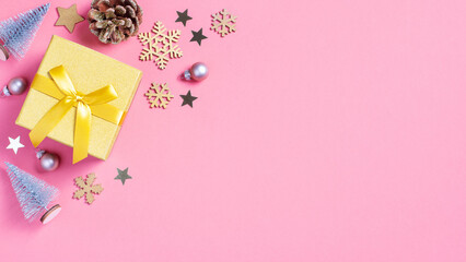 Christmas golden gift box with mini Christmas trees and baubles on pastel pink background