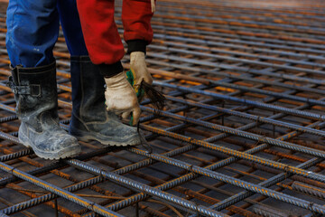 Worker welds reinforcing mesh. Male workers are working on a retaining wall, knitting rebar and...