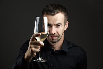 Portrait of smiling man in a black shirt with wine glass in hand on dark background. Portrait of young caucasian dark-haired man
