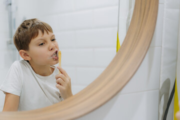 cute 8 years old boy washing face in bathroom looking in mirror and smiling.
