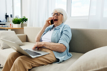 laughing loudly during a phone conversation with her family, an elderly lady is sitting relaxed on...