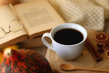 Cup of tea or coffee, seasonal spices, bowl of cookies, blanket, pumpkins, colorful leaves, books and tangerines on wooden table. Cozy hygge at home. Selective focus.