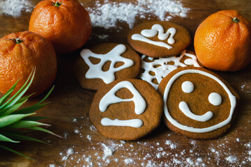 Sweet gingerbread cookies covered with white icing with various patterns, surrounded by tangerines and part of a green plant on a board with flour