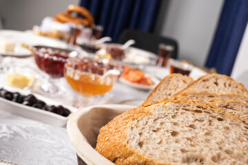 Whole wheat bread, selective focus and close up of sliced whole wheat bread. Traditional Turkish breakfast table blurred background. Olive, jar, tomatoes, glass of tea. 