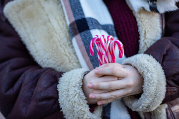 Mujer agarrando bastones de caramelo mientras pasea por Madrid abrigada con abrigo y bufanda en...