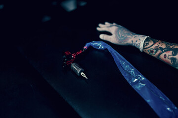 Hand tattooist in white gloves with upper tattoo machine against bed on black background.