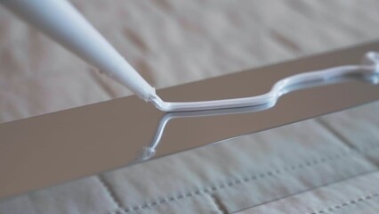 Top view shot of white glue applying on metal profile surface, workman applying sealant in zig zag for further installing. Repairing adhesive glue for fixing different types of surface, industrial