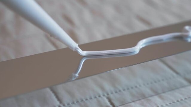Top view shot of white glue applying on metal profile surface, workman applying sealant in zig zag for further installing. Repairing adhesive glue for fixing different types of surface, industrial