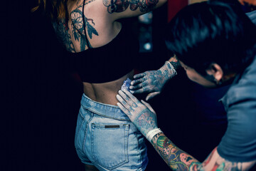 Close-up hands of master Tattoo artist in white gloves sticking paper with pattern on client hand on a girl's waist, in a modern studio lowlight.