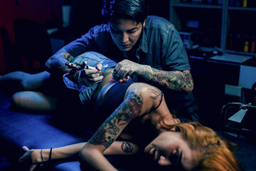 Obraz na płótnie Canvas Professional tattooist makes the tattoo on a girl waist, focusing on tattoo machines in a modern studio lowlight.