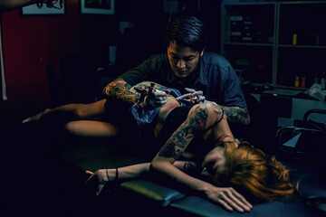 Professional tattooist makes the tattoo on a girl waist, focusing on tattoo machines in a modern studio lowlight.