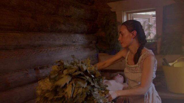Slow motion of professional bath attendant over body of sauna visitor. Therapeutic procedures using hot air. Use of useful aromatic substances contained in oak brooms