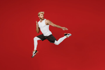 Fototapeta na wymiar Full body side profile view young strong sporty toned sportsman man wear white clothes spend time in home gym run jump high look aside isolated on plain red background Workout sport fit body concept.