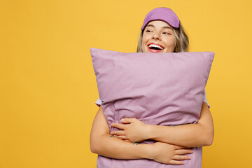 Fun young woman she wears purple pyjamas jam sleep eye mask rest relax at home hold pillow look...