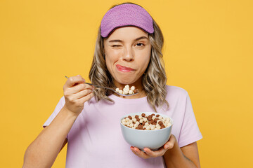 Young woman in purple pyjamas jam sleep eye mask rest relax at home eat breakfast muesli cereals...