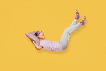 Full body side view young woman she wears purple pyjamas jam sleep eye mask rest relax at home fly up hover over air fall down on pillow isolated on plain yellow background studio. Night nap concept. - obrazy, fototapety, plakaty