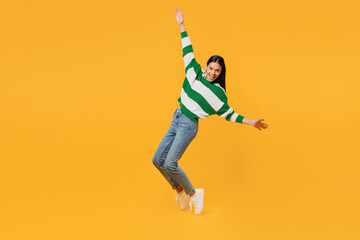 Fototapeta na wymiar Full body side view young latin woman wear casual cozy green knitted sweater stand on toes leaning back dance with outstretched hands look camera isolated on plain yellow background studio portrait.