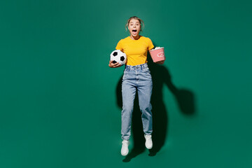 Naklejka na ściany i meble Full body young woman fan wear yellow t-shirt cheer up support football sport team eat popcorn hold in hand takeaway bucket soccer ball watch tv live stream isolated on dark green background studio.