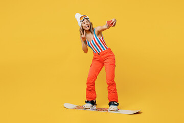 Snowboarder woman wear orange ski suit goggles mask hat swimsuit spend extreme weekend doing selfie...