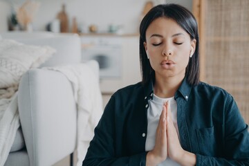 Female breathing deep, listens to meditation in earphone with namaste gesture at home. Stress relief