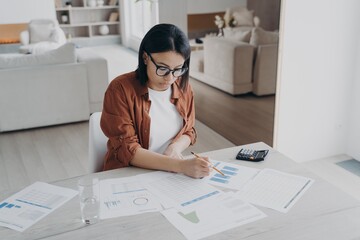 Female freelancer analyzing financial documents, calculates expenses, works on project at home - obrazy, fototapety, plakaty