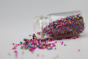 Colorful glitters in a small glass bottle isolated on white background. Closeup of a glitter glass jar. Beautiful still life vintage concept. Multicolor glitters.