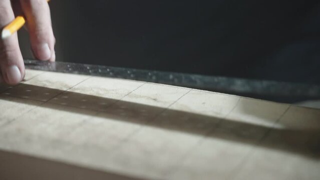 Professional carpenter using pencil and metal ruler for making measurements on wood plant surface before cutting. Thick timber plank in workshop, jointer drawing lines dividing wood surface on equal