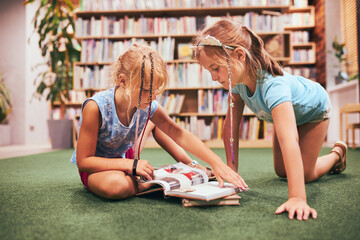 Two schoolgirls reading books in school library. Primary school students learning from books....