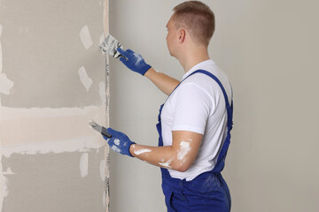 Man plastering wall with putty knife indoors. Home renovation