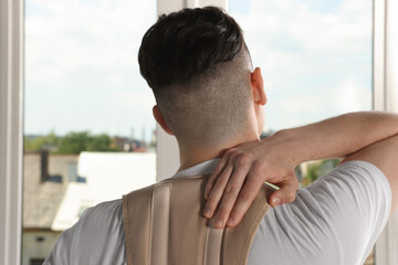 Man with orthopedic corset near window indoors, back view