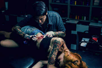 Professional tattooist makes the tattoo on a girl waist, focusing on tattoo machines in a modern studio lowlight.