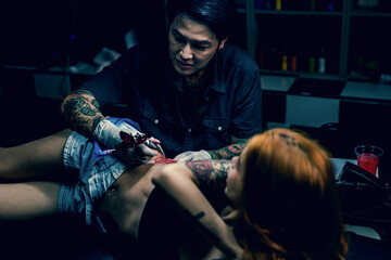 Professional tattooist makes the tattoo on a girl waist, focusing on tattoo machines in a modern studio lowlight.