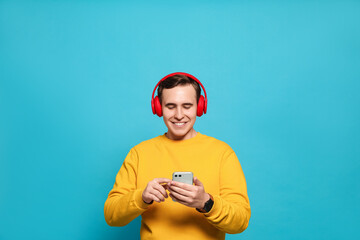 Naklejka premium Handsome young man with headphones and modern smartphone on light blue background