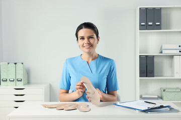 Beautiful female orthopedist showing insoles at table in hospital