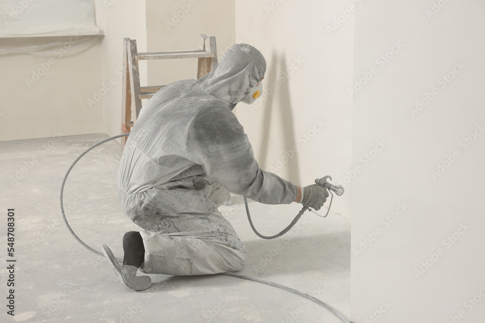 Canvas Prints Decorator in protective overalls painting wall with spray gun indoors