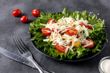 Traditional caesar salad with chicken on a black plate on black table with napkin fork and knife.