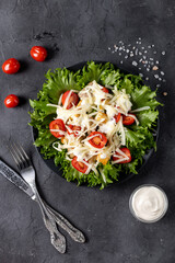 Traditional caesar salad with chicken on a black plate on black table with napkin fork and knife.