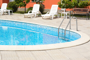 Outdoor swimming pool with handrails and empty sunbeds at resort on sunny day