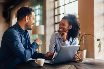 Happy woman and man being at the office, having a meeting, using a laptop.
