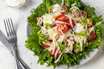 Traditional caesar salad with chicken on a plate on white table with napkin fork and knife.
