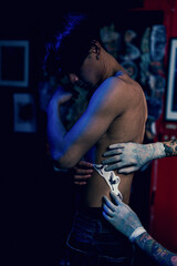 Fototapeta na wymiar Close-up hands of master Tattoo artist in white gloves sticking paper with pattern on client hand on a Man waist, in a modern in Studio lowlight.